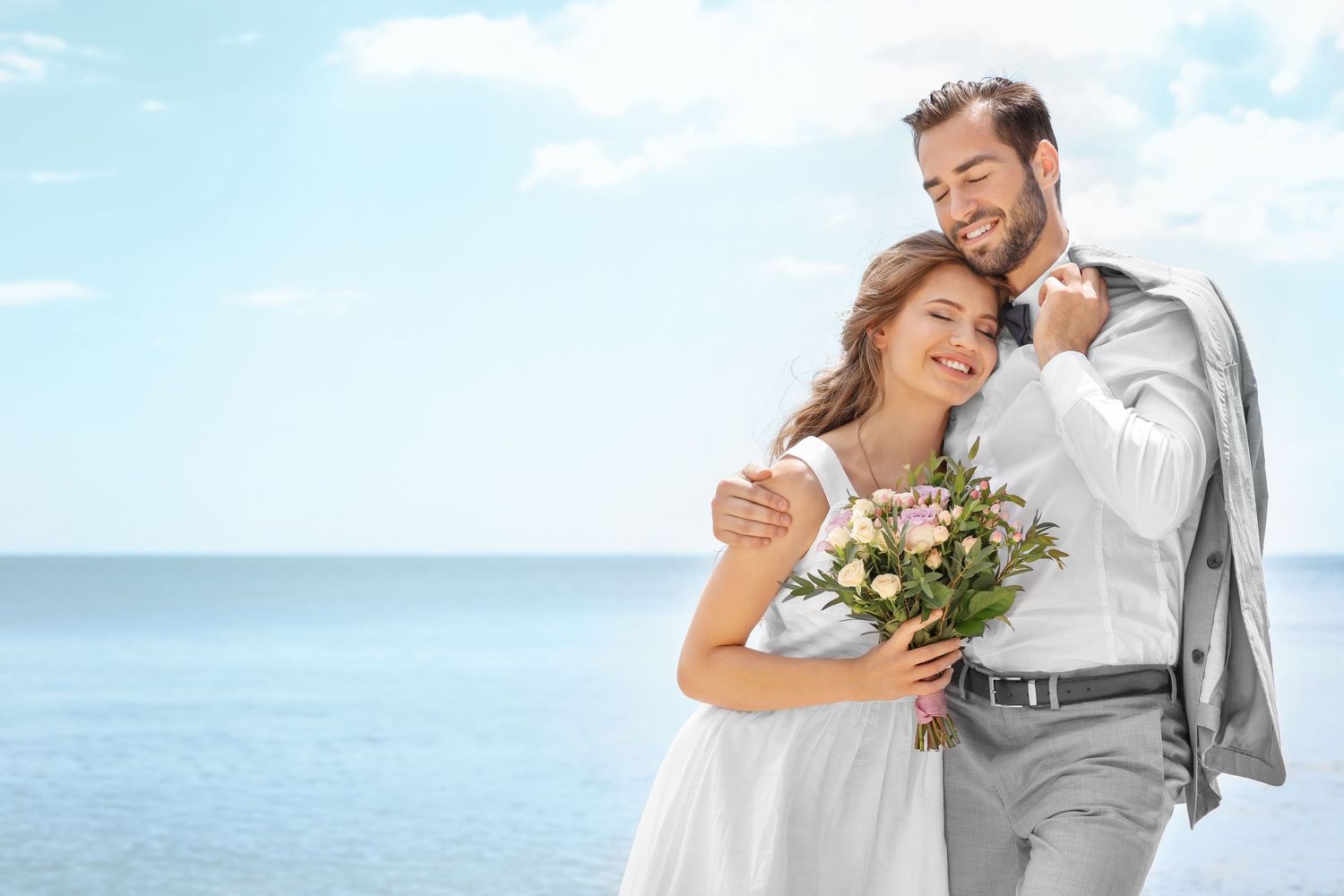 A romantic couple embracing outdoors against an ocean backdrop with flowers.