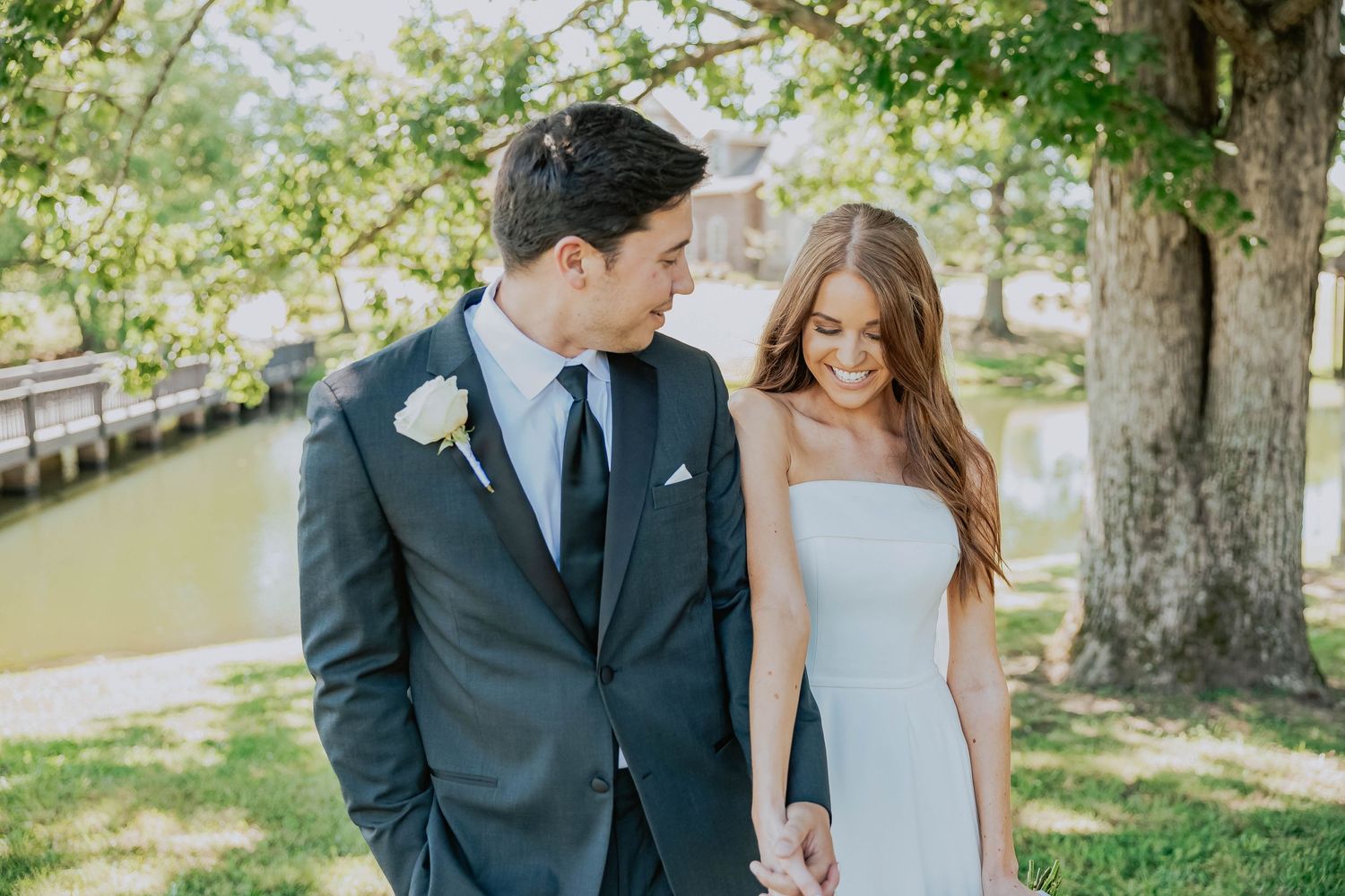 A romantic outdoor photoshoot with a couple in formal attire under green trees.