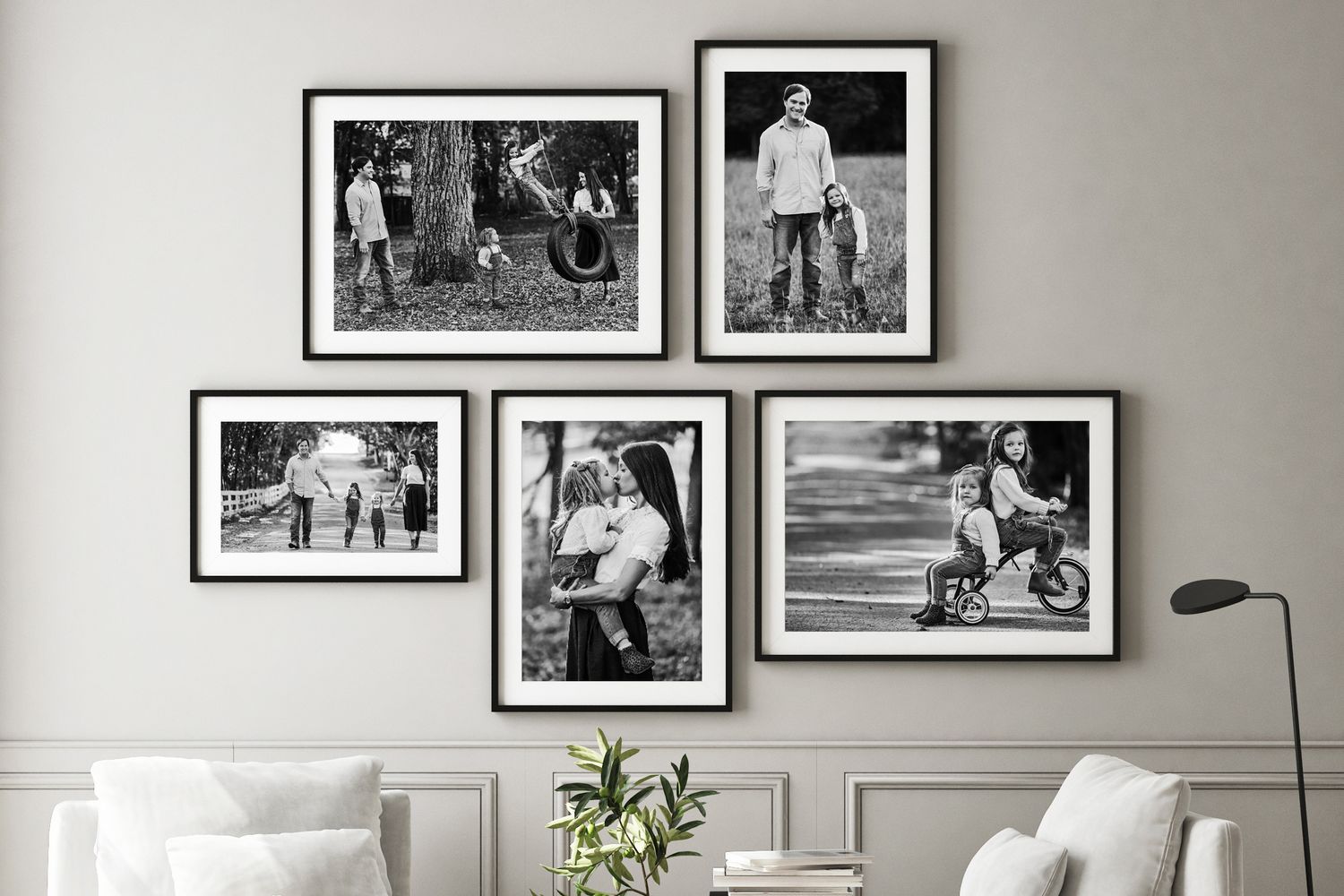 Black and white family photos arranged in frames on a gray wall above white furniture.