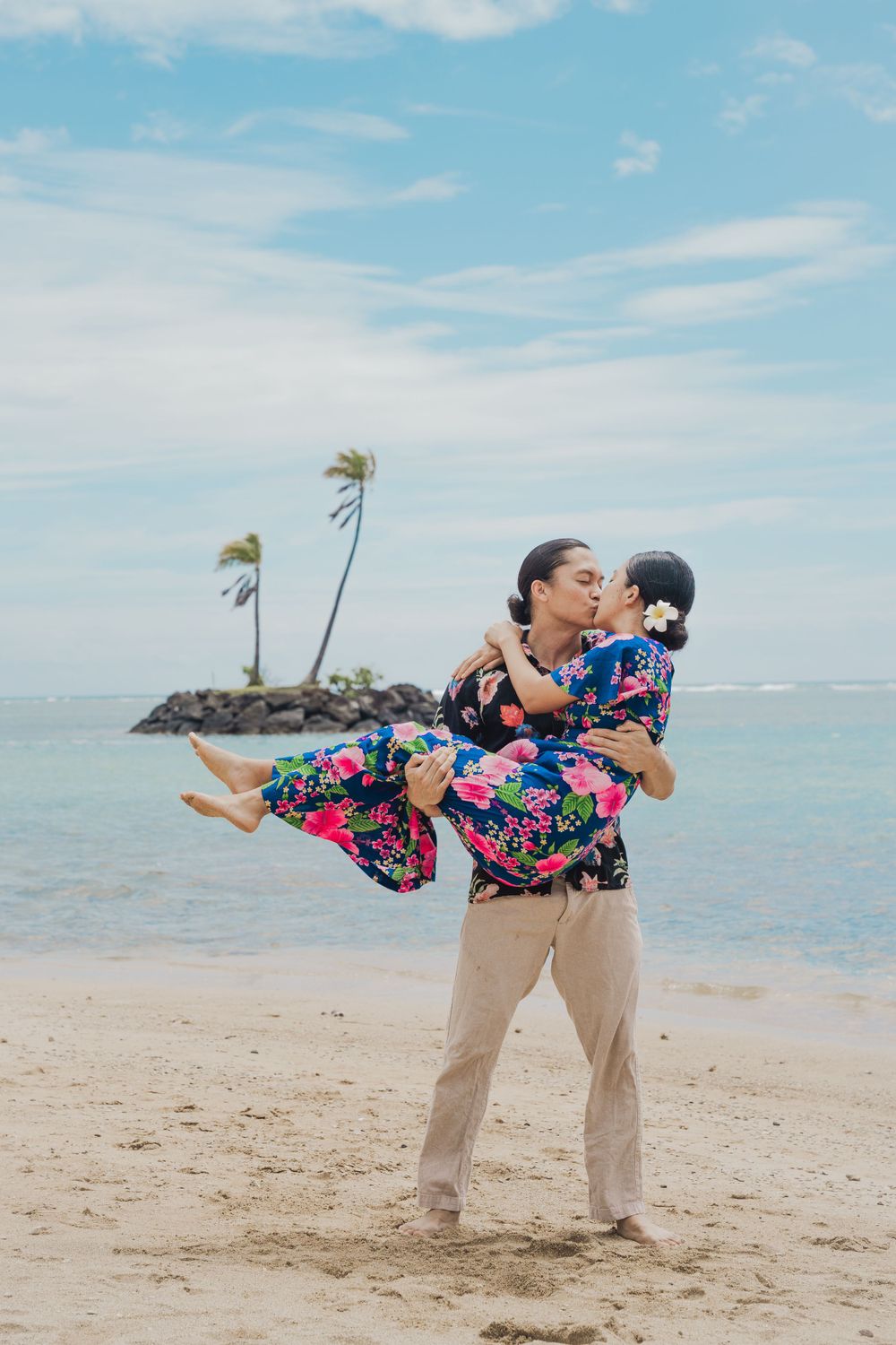 A romantic scene unfolds on a Hawaiian beach with palm trees and ocean views as a couple shares a playful moment.