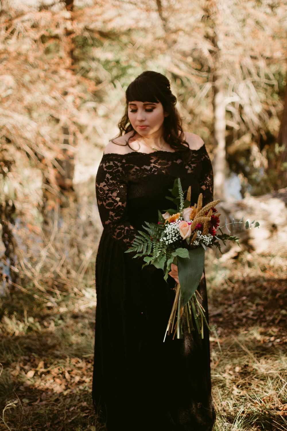 A romantic outdoor portrait with black lace dress and rustic autumn bouquet in warm lighting.