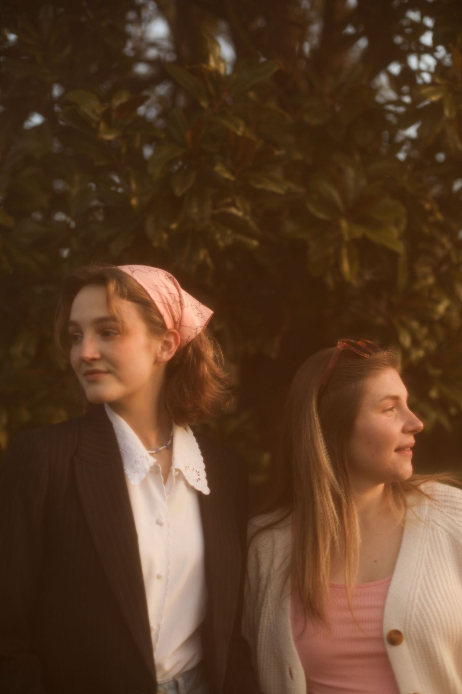 Two people in vintage-inspired outfits with headscarves posed against foliage.