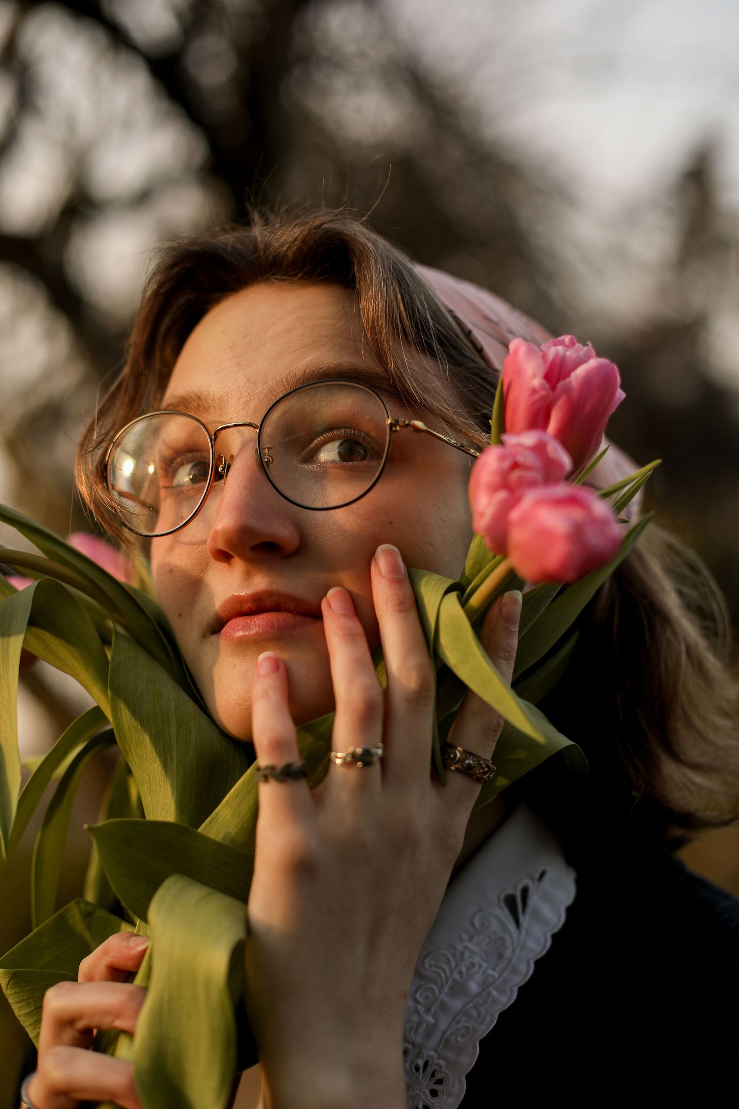 Portrait of person with glasses holding pink tulips against moody evening light.