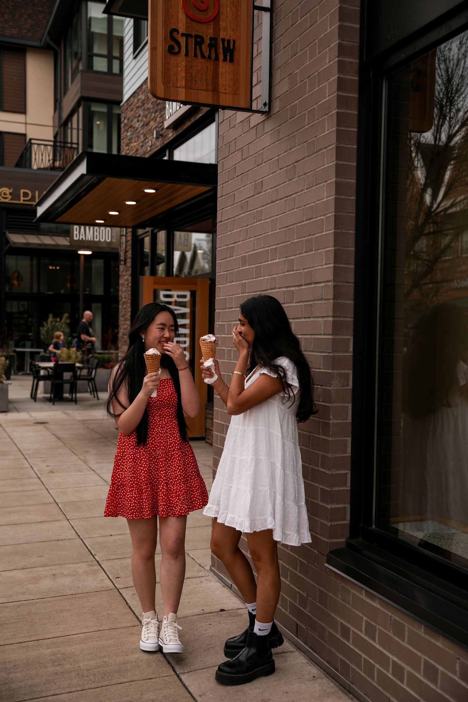Two friends enjoying drinks outside a cafe with 'Straw' signage on brick building.