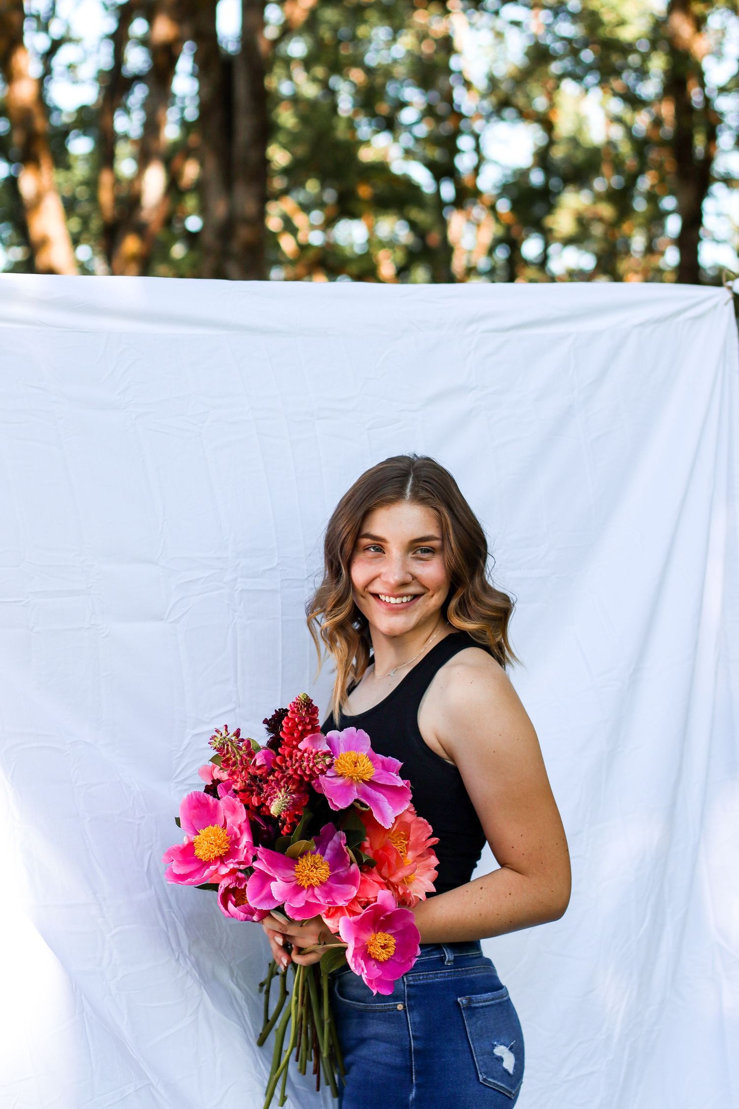 Person holding vibrant pink and red flower bouquet against white backdrop outdoors.