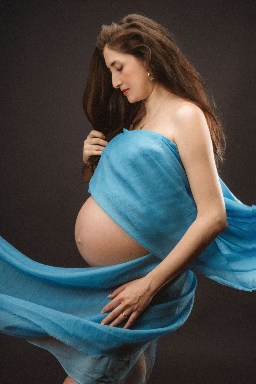 Artistic maternity portrait with flowing blue fabric against dark background.