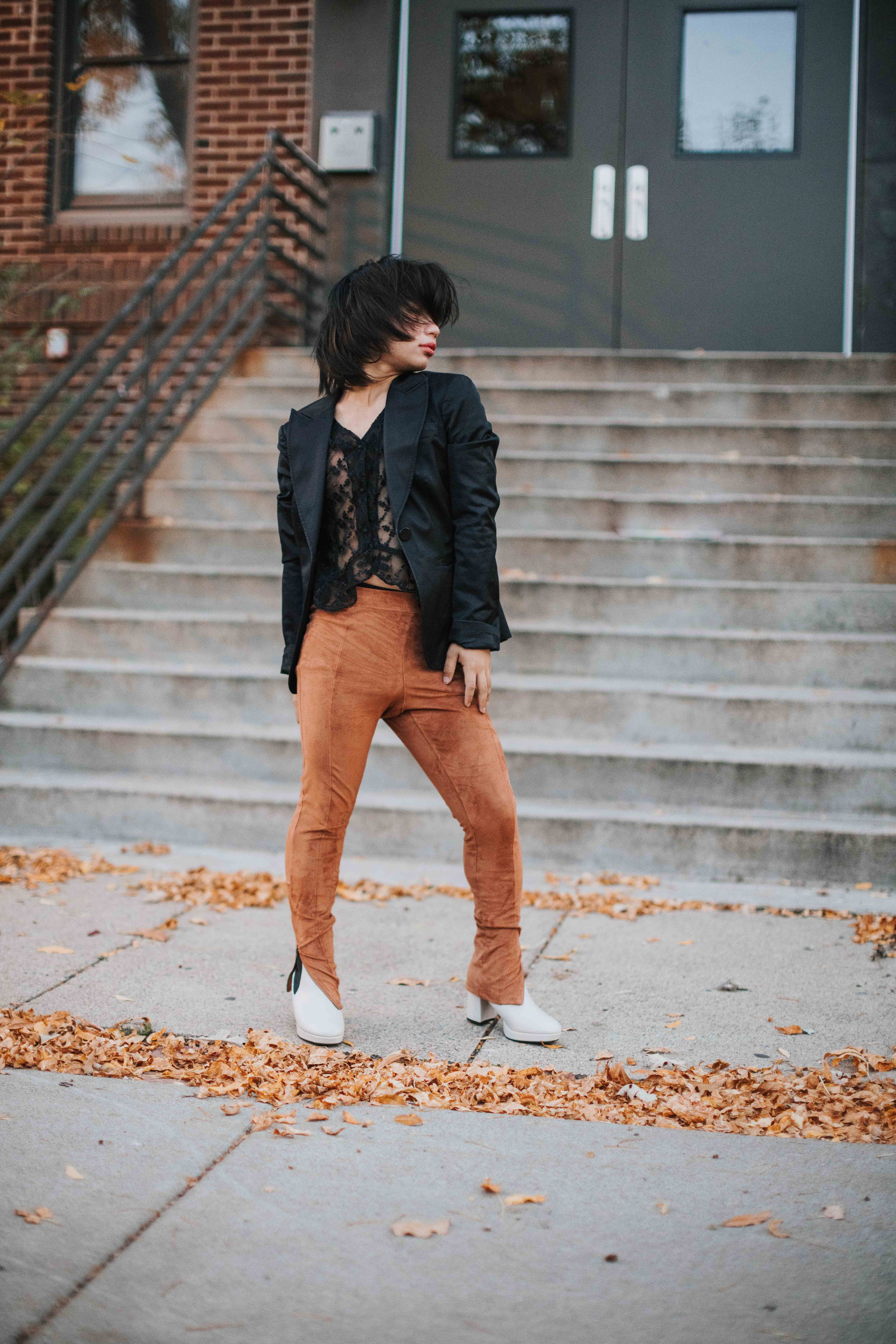 Fashion photo of person in orange pants and black jacket posing on steps with fallen autumn leaves.