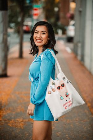 Casual street style outfit with blue dress and white tote bag on autumn sidewalk.