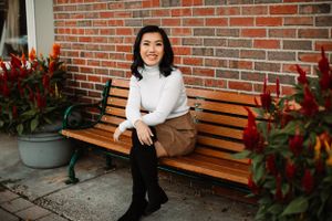 Casual autumn outfit with white turtleneck and brown pants on wooden bench by brick wall.