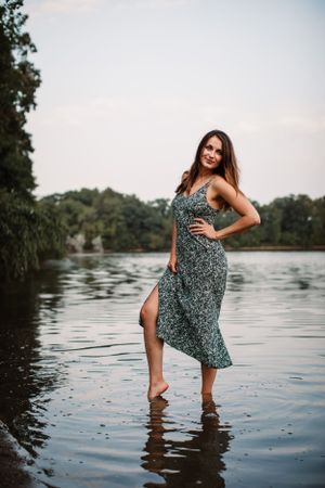 Woman in patterned dress stands in shallow water at sunset.