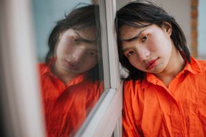 Artistic reflection portrait in orange shirt against window glass.