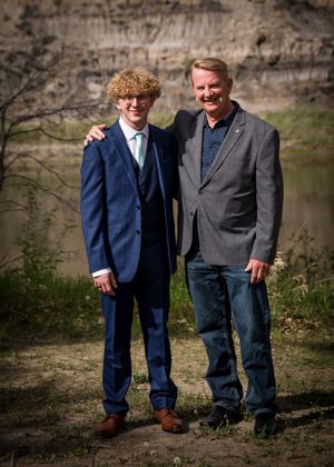 Two people standing together outdoors in formal attire near a riverbank.