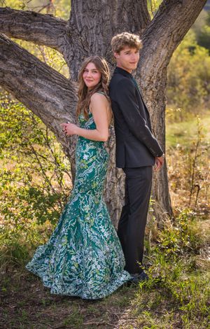 Formal couple poses together against large tree trunk in outdoor setting.