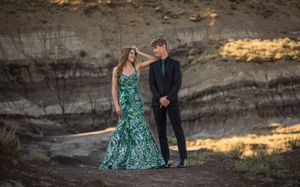Couple poses against rocky cliffs in formal attire with emerald green gown and dark suit at sunset.
