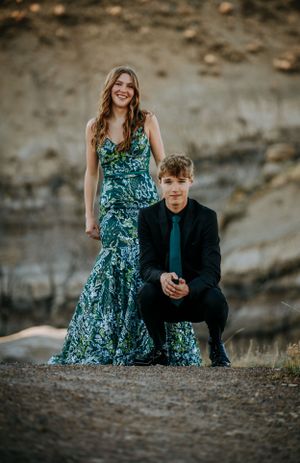Formal portrait of couple with emerald dress and dark suit against rocky landscape.