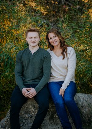 Two people in sweaters sitting together on rock with beautiful fall colors in background.