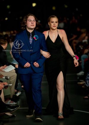 A couple models formal attire on a runway - navy suit and black evening dress.