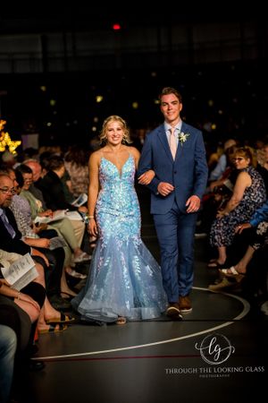 A couple walks the runway in formal wear - blue sequined gown and navy suit.