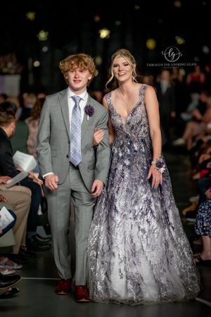 Formal couple walks runway with woman wearing sparkly gray ball gown and man in light gray suit.