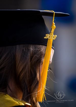 Close-up detail of graduation cap with bright yellow tassel against dark background.