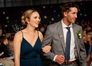 Couple walks runway together, woman in navy dress and man wearing gray suit with blue tie.