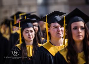 Graduates in black caps and gowns with yellow stoles stand together during commencement ceremony.