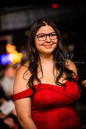 A woman in a red off-shoulder dress smiles warmly while wearing glasses at an elegant event.