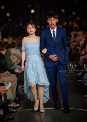 A couple walks the runway, with her in a blue lace dress and him in a navy suit.