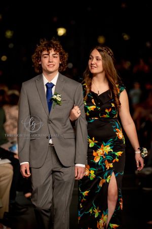 A couple poses on a runway, with him in a grey suit and her in a floral print dress.
