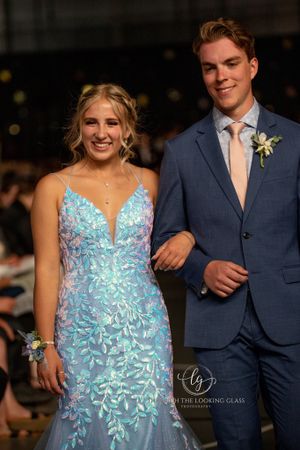 A couple walks the runway with her in a sparkly blue gown and him in a navy suit with boutonniere.
