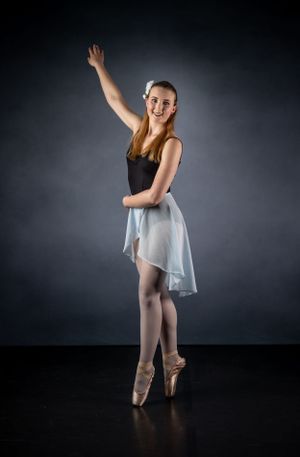 A graceful ballet dancer poses en pointe wearing a light flowing skirt against dark backdrop.