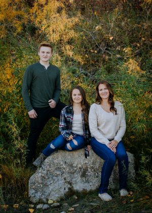 Family portrait of three people sitting on a large rock with golden autumn foliage backdrop.