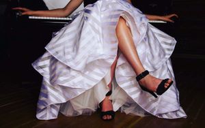 Close-up of formal dress hemline and black strappy heels on a dark stage.