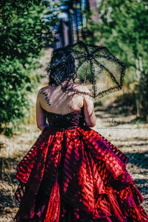 Gothic-inspired portrait featuring dramatic red ball gown and black lace parasol in a garden setting.
