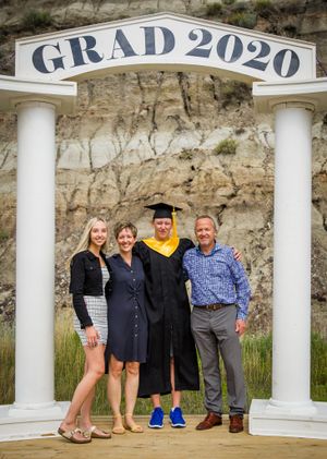 A family poses under a 'GRAD 2020' archway with white columns against a stone wall backdrop.