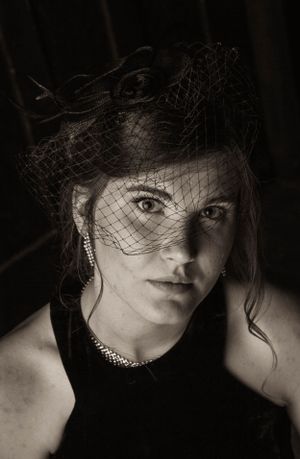 Vintage-style portrait with dark veil and necklace creating dramatic film noir aesthetic.