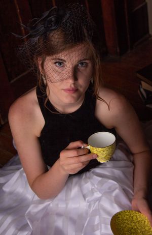 A woman in vintage attire poses with a yellow teacup against white fabric.