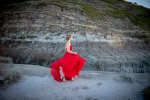 Figure in flowing red gown twirling against dramatic rocky cliffside.