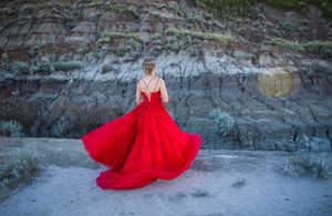 Stunning red ballgown billowing dramatically against layered rock formations.