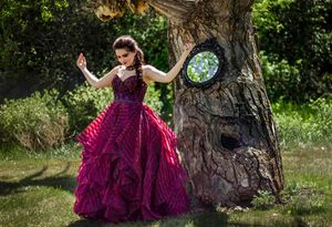Enchanting fairy tale scene with burgundy gown and decorated tree in sunny garden.