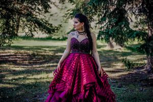A dramatic burgundy ball gown worn in an outdoor garden setting with trees in the background.