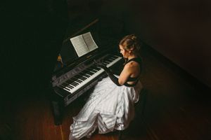 An elegant figure in a contrasting black and white gown sits at a grand piano in dim lighting.
