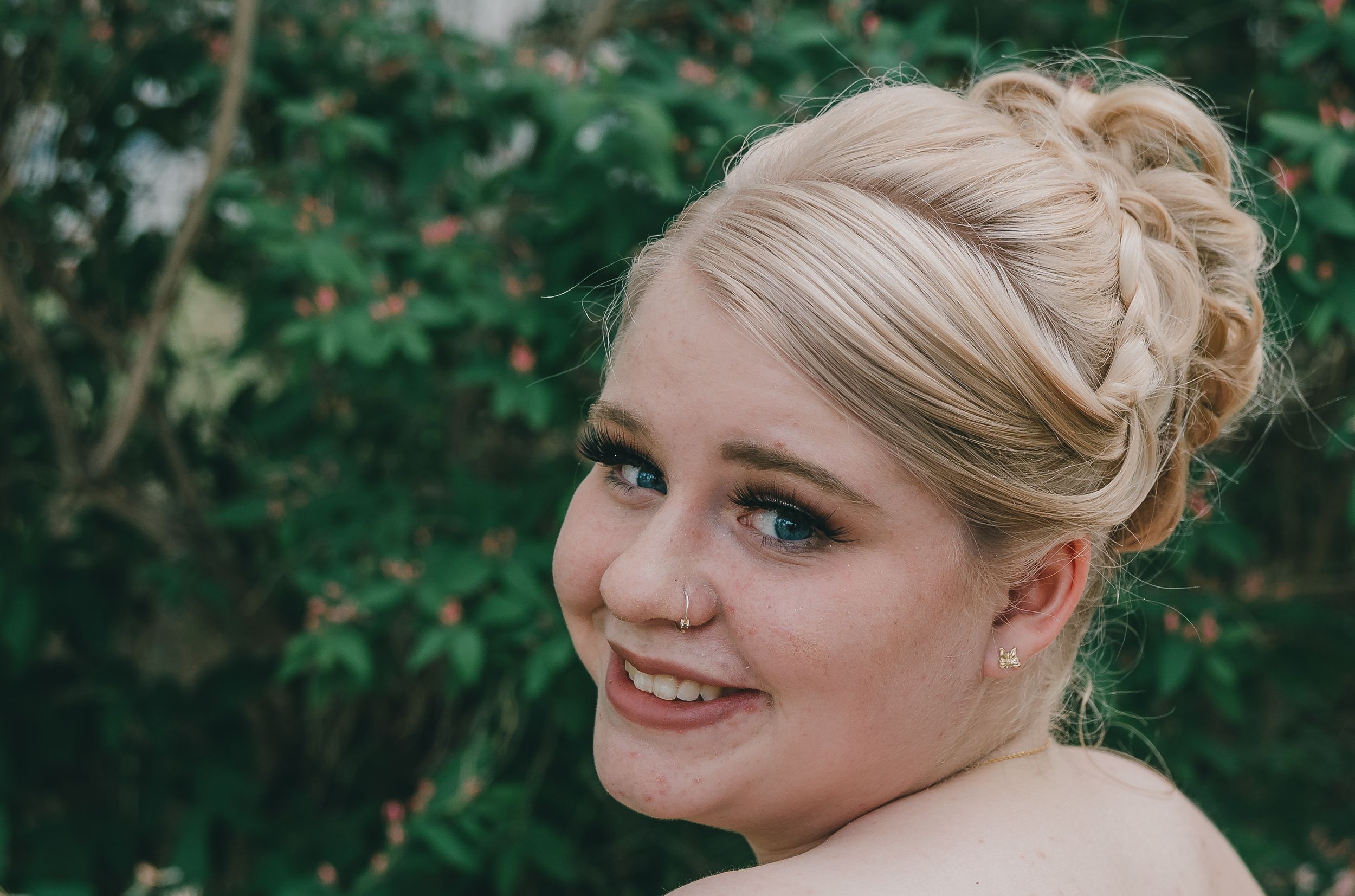 A close-up portrait outdoors with natural greenery in the background.