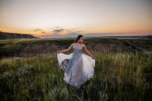 A flowing white dress twirls against a scenic sunset backdrop in an open field.