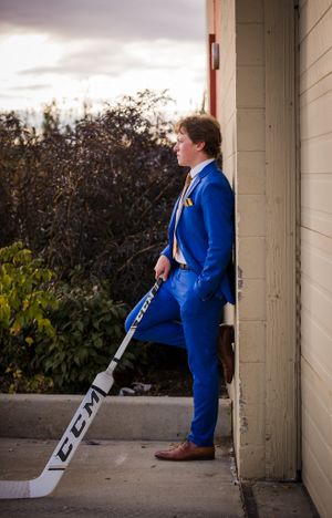 A person in a bright blue suit poses with a hockey stick against a building wall.