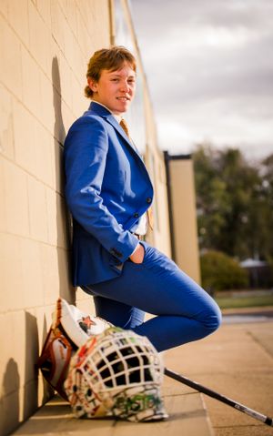 Formal portrait with hockey gear showing someone in a vibrant blue suit against a light wall.