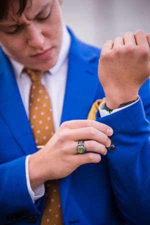 Close-up of hands adjusting cufflinks on a bright blue suit with gold polka dot tie.