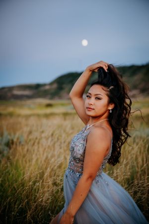 Portrait of woman in embellished gray gown posing in field with moon in background.