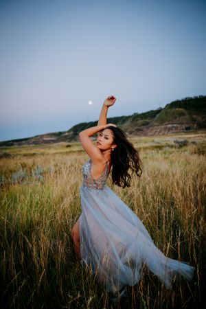 A flowing light blue gown swirls gracefully in a golden field at sunset with mountains in the background.