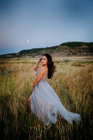 Elegant blue dress flowing in wind against backdrop of tall grass and dusky sky.